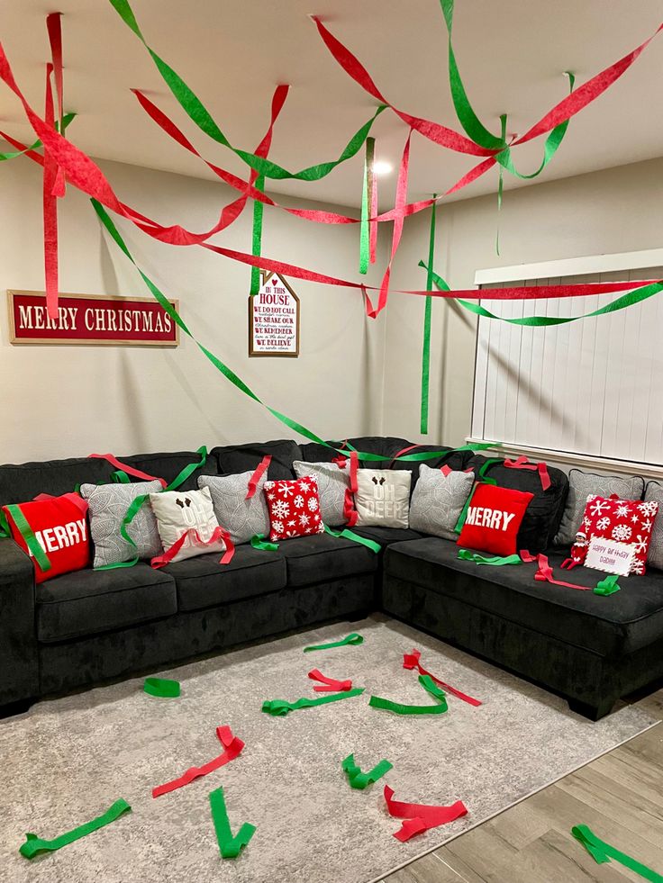 a living room decorated for christmas with red and green streamers on the ceiling, black couches, and white rugs