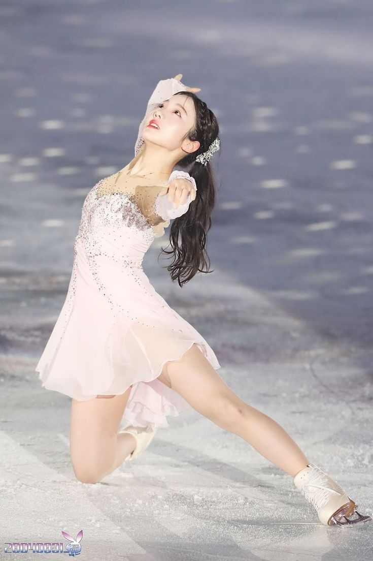 a female figure skating on ice in a white dress and tiara, with her arms stretched out