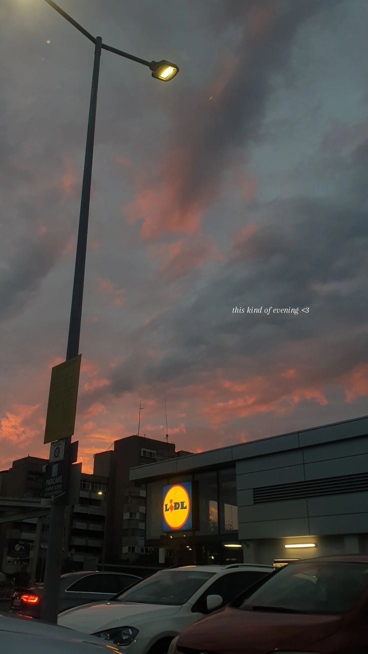 cars are parked on the street in front of a building with a sign that says, this is an awesome evening sky