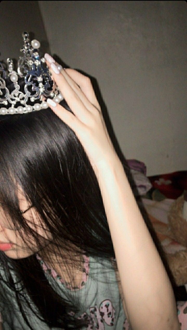 a woman wearing a tiara and holding her hair in front of her face with both hands