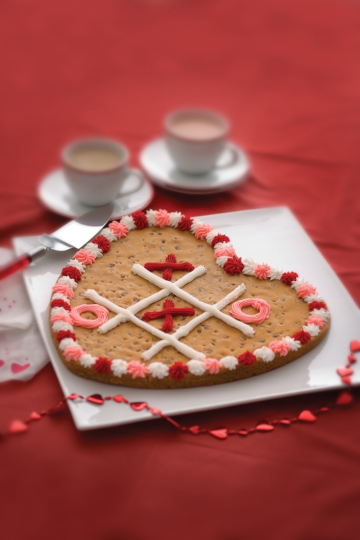 a heart shaped cookie on a plate with two cups and saucers in the background