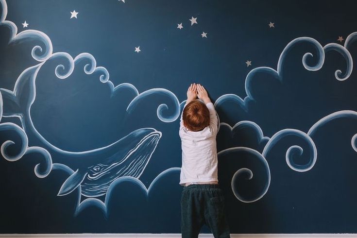 a young boy is painting a mural on the wall with stars and clouds above him