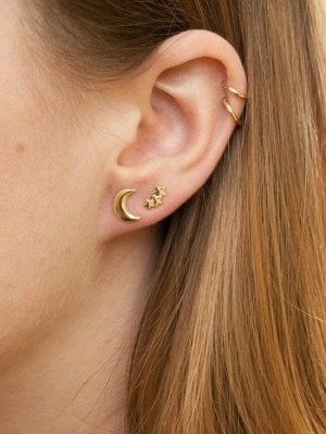 a close up of a person with ear piercings on their ears and wearing gold jewelry