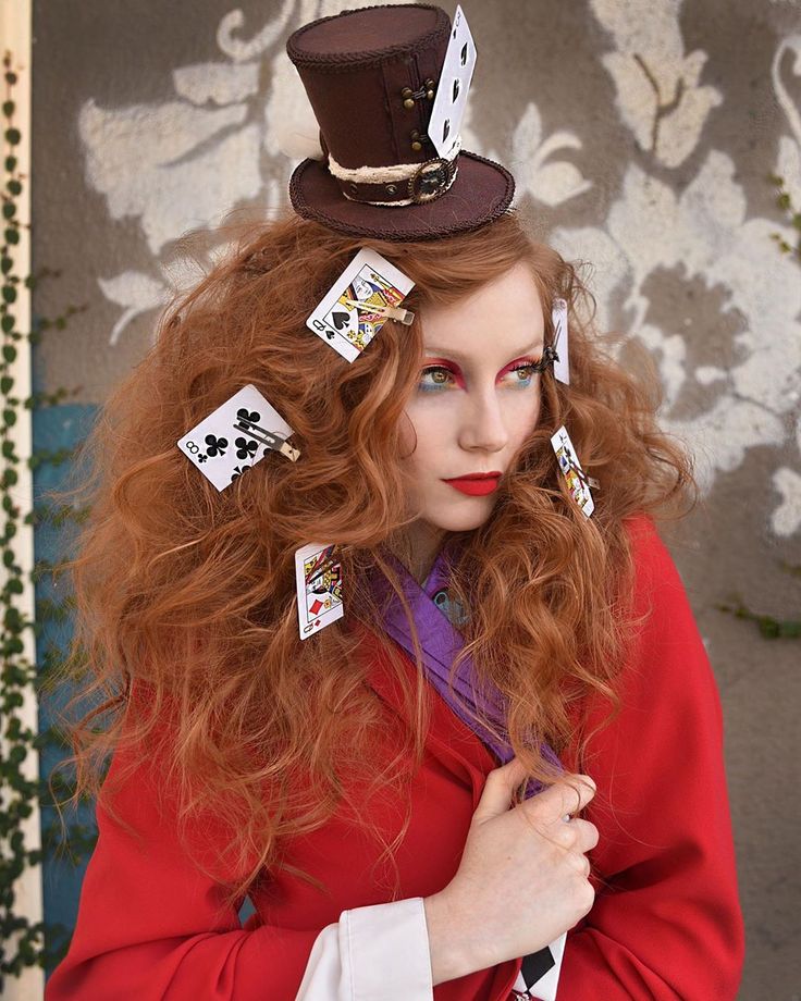 a woman with long red hair wearing a top hat and playing cards on her head