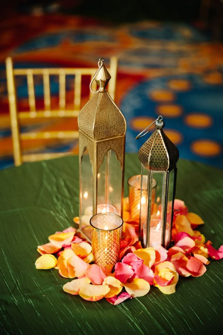 two lit candles are sitting on a green tablecloth with flowers and petals around it