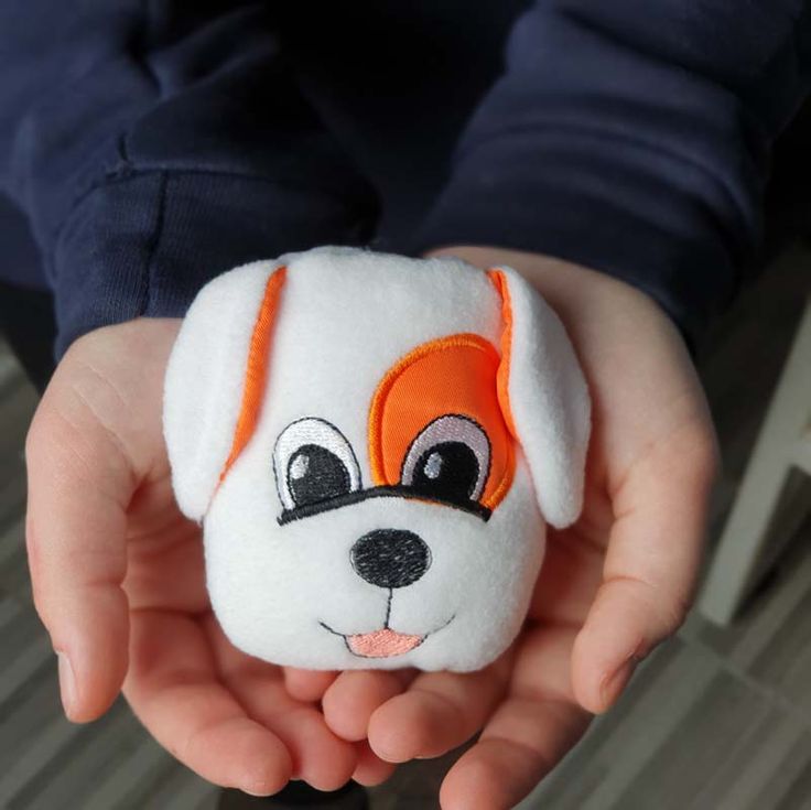 a person holding a small stuffed animal in their hands with an orange and white dog on it's face