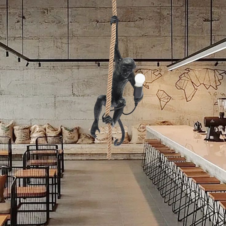 a monkey hanging from a rope in an industrial restaurant with tables and chairs around it