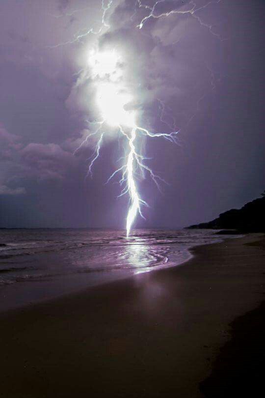 a lightning bolt hitting over the ocean on a beach at night with clouds in the background