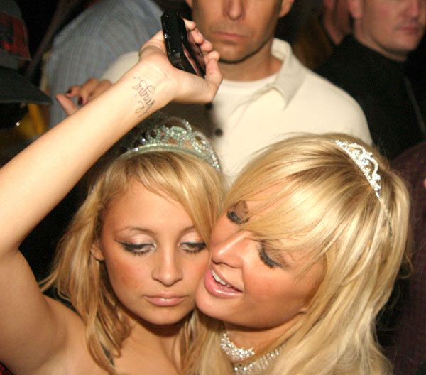 two beautiful young women standing next to each other in front of a man holding a cell phone