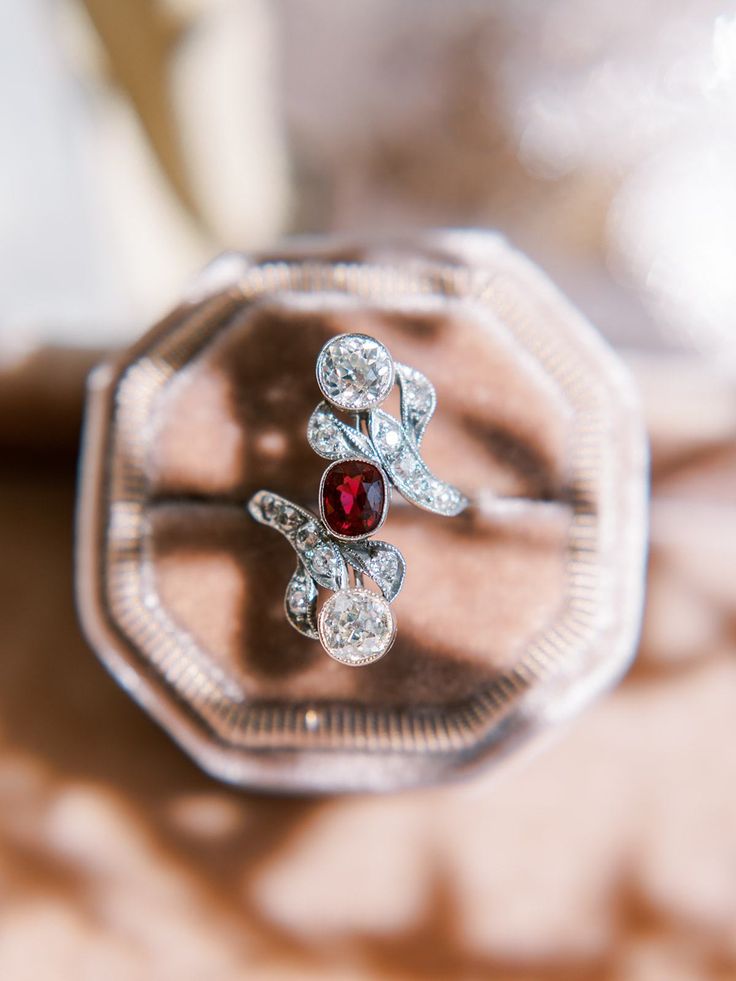 an engagement ring with two diamonds and a garnet colored stone sits on a table