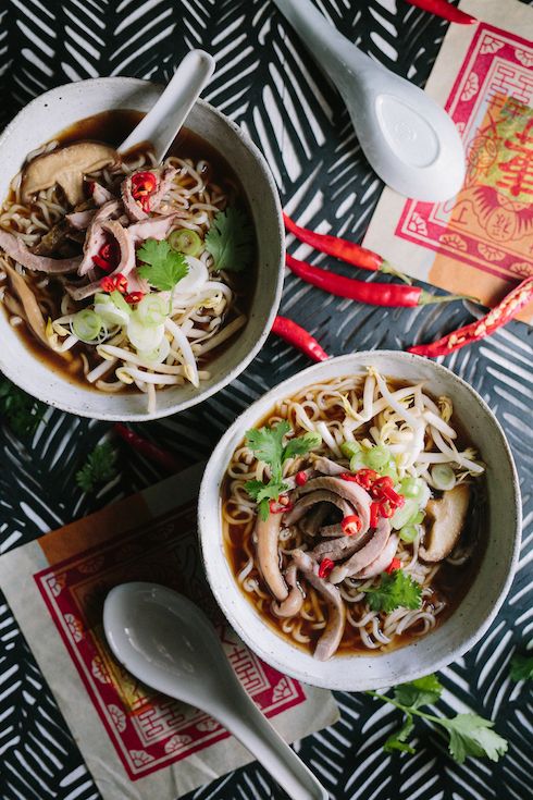 two bowls filled with noodles and vegetables on top of a table next to chopsticks