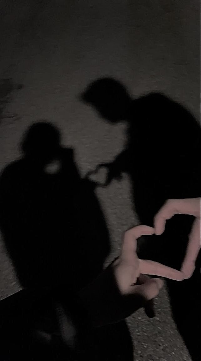 two people standing next to each other in the dark with their shadows on the ground