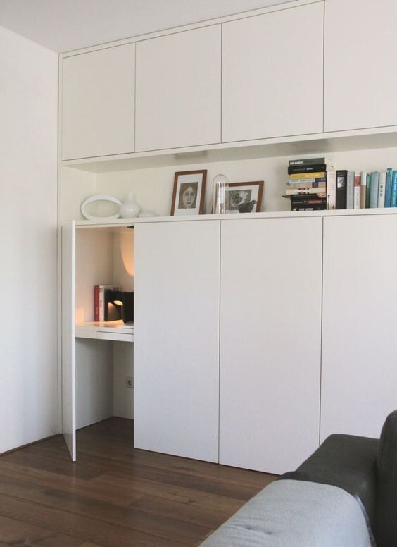 a living room filled with furniture and lots of white cupboards next to a window