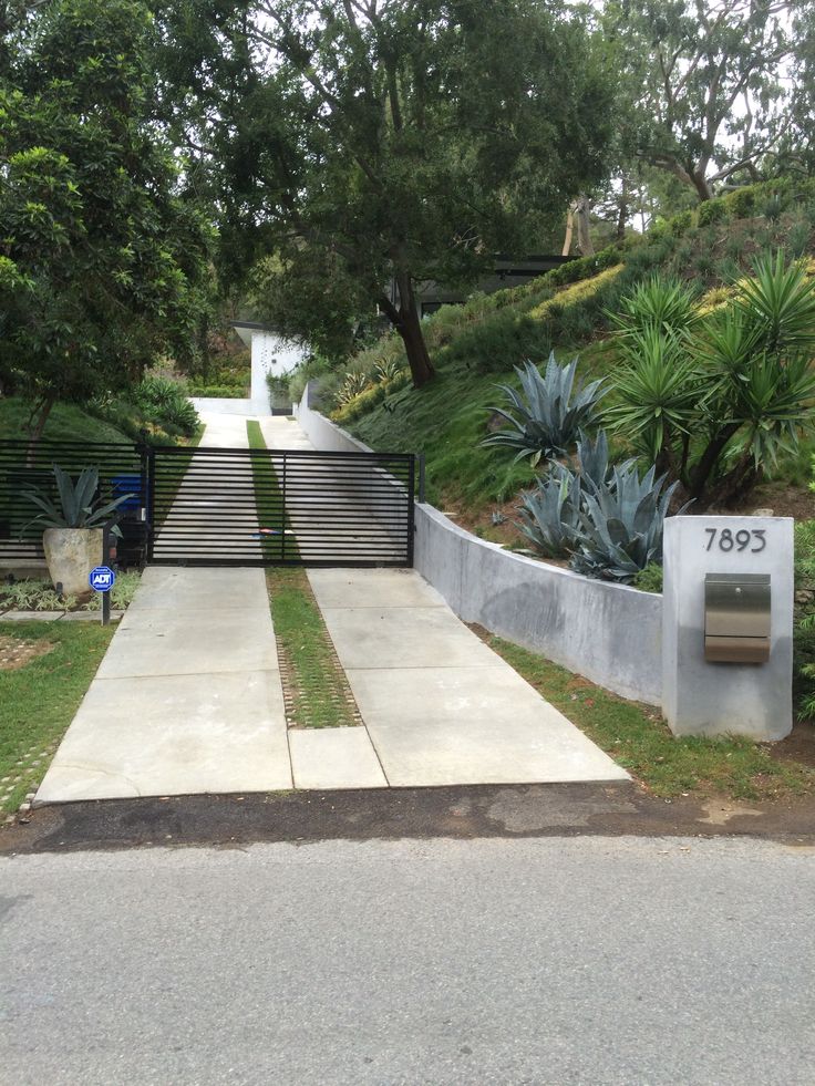 a concrete walkway leading to a gated in area with trees and bushes on both sides