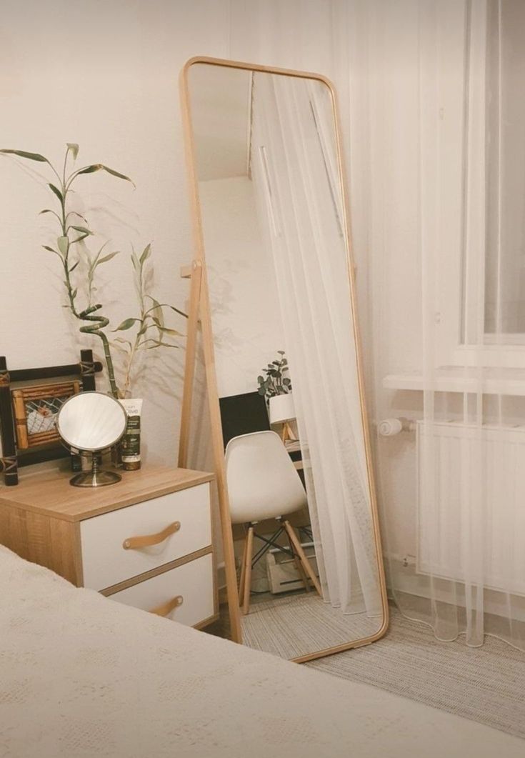 a mirror sitting on top of a wooden dresser next to a white bed in a bedroom