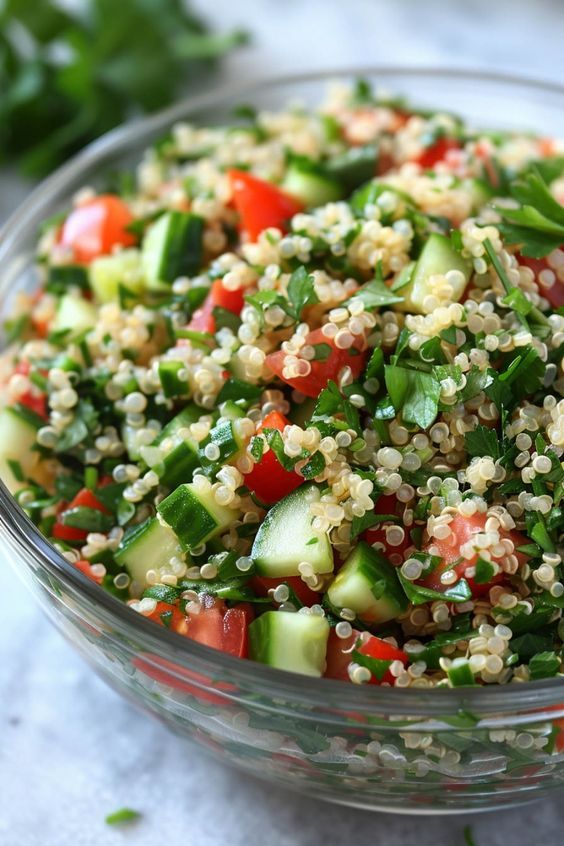 a glass bowl filled with cucumber, tomato and couscouse salad