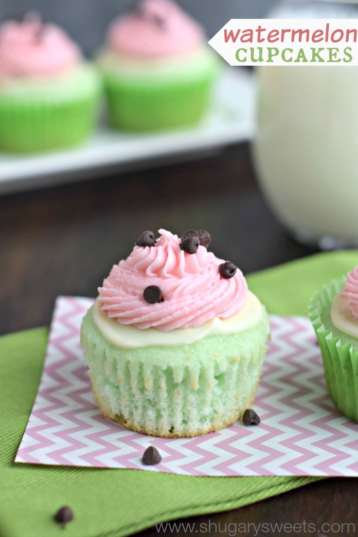 two green cupcakes with pink frosting and chocolate chips on top, next to a glass of milk