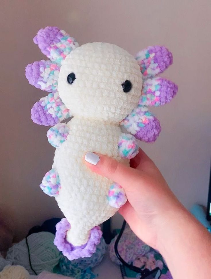 a hand holding a small white and purple stuffed animal