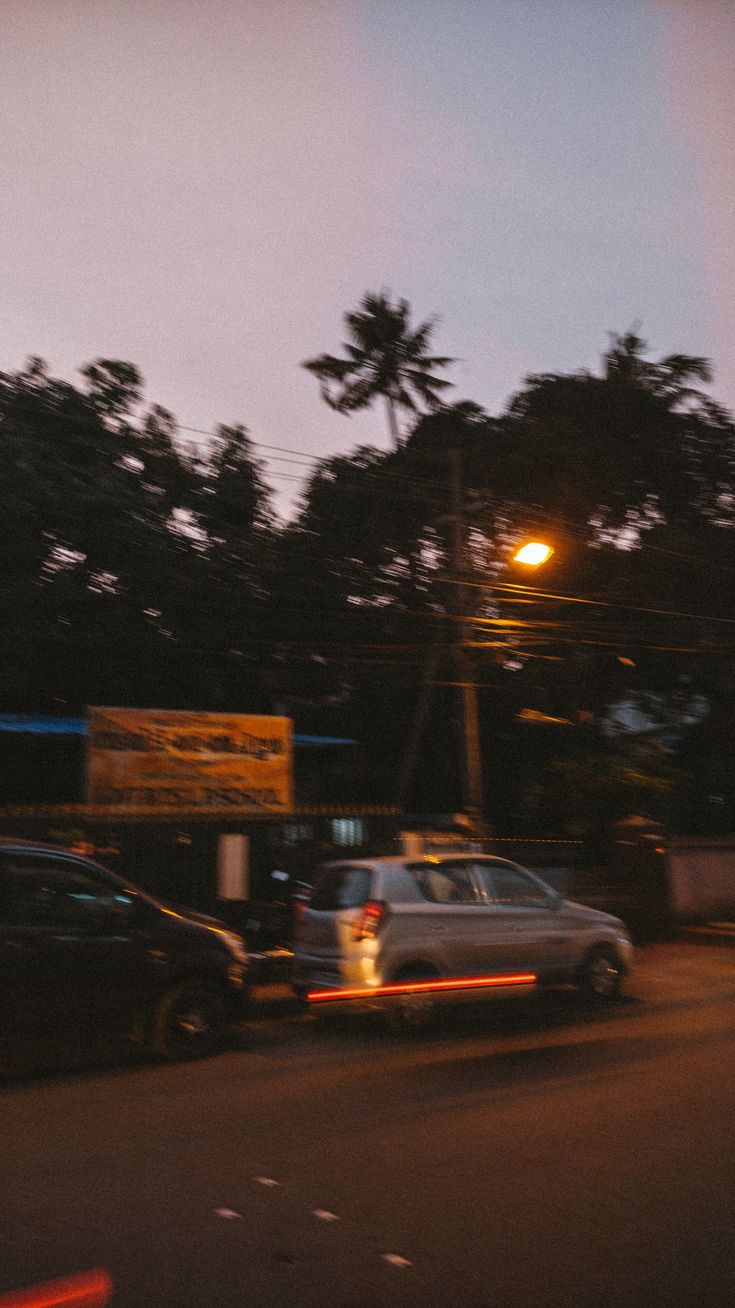 cars are parked on the side of the road at night with trees in the background