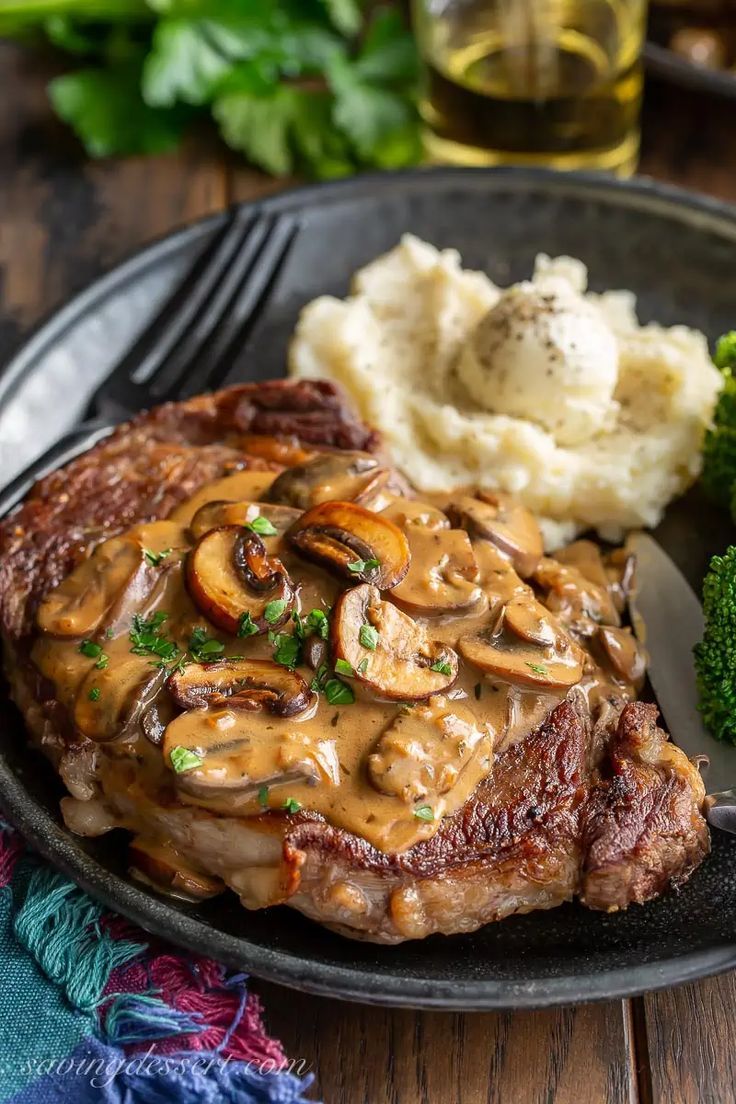 steak with mushroom gravy and mashed potatoes on a plate next to broccoli