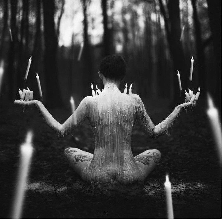 a woman sitting in the middle of a forest with candles floating from her hands,