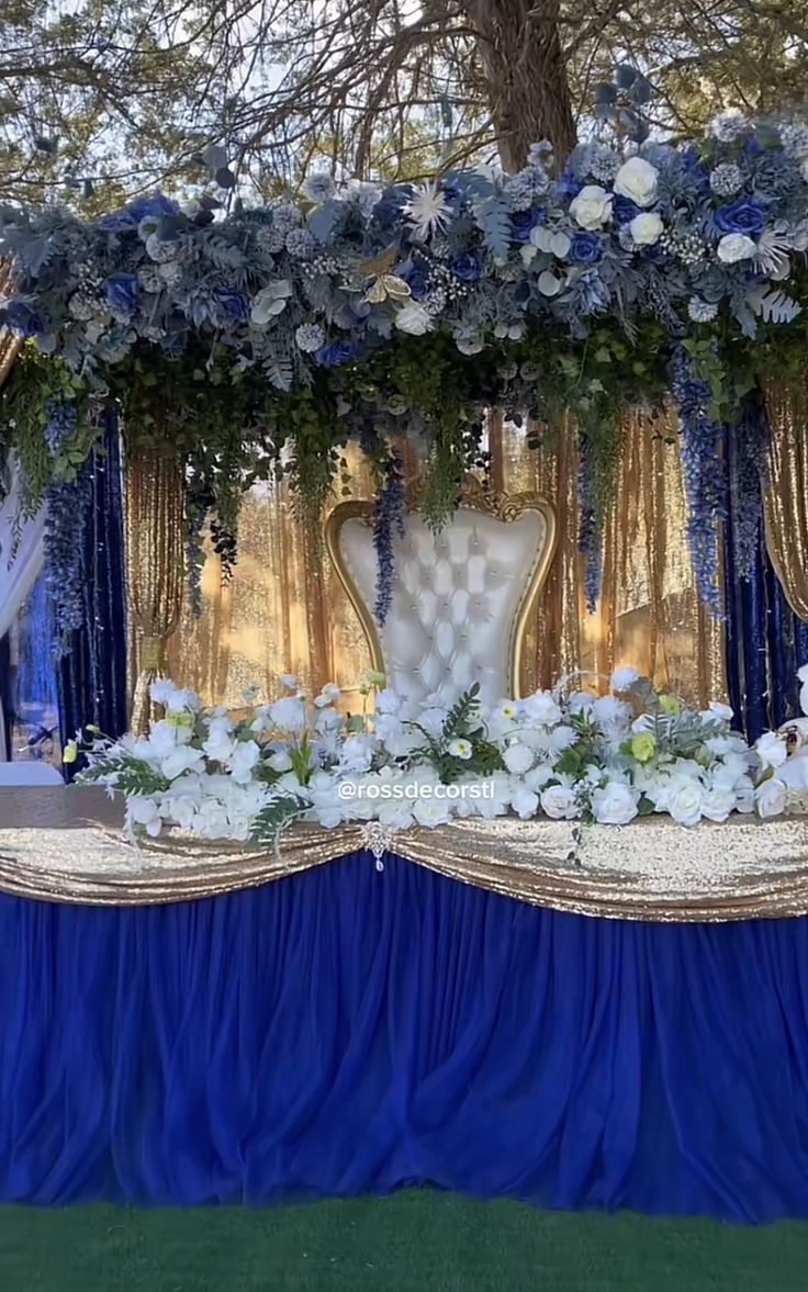 a blue and white wedding setup with flowers on the head table, draped in gold cloths