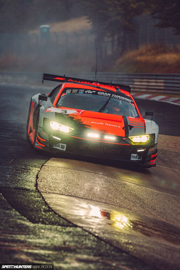 a race car driving on a wet track at night time with fog coming from behind it