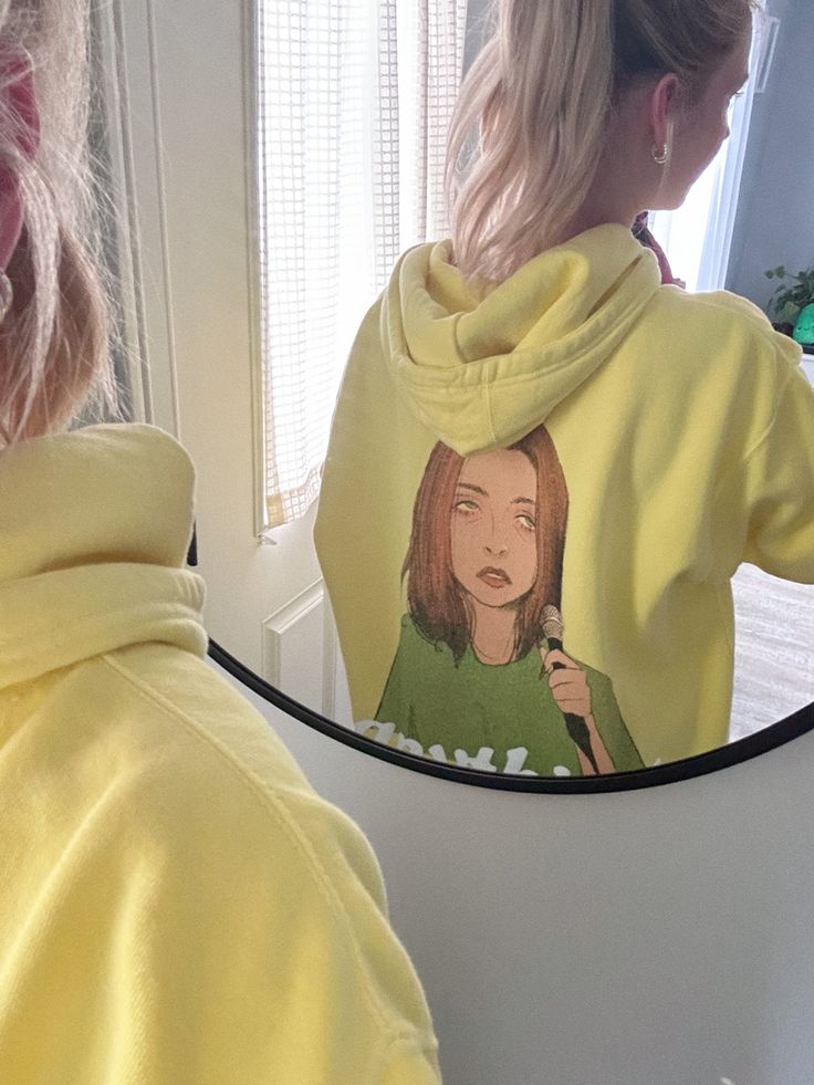 a woman in a yellow hoodie is brushing her hair with a blow dryer