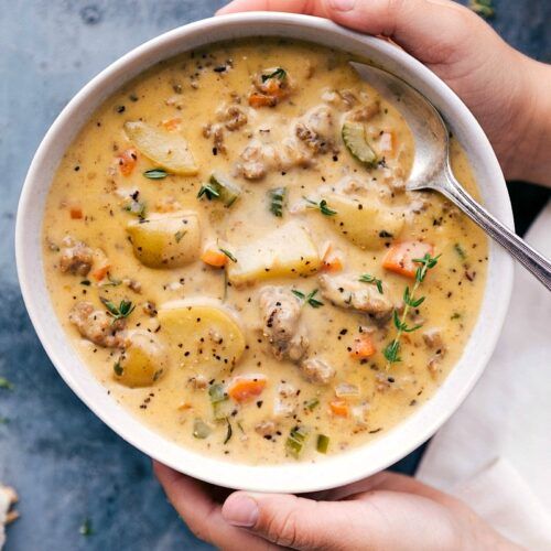 two hands holding a bowl of chicken and dumpling soup on a blue tablecloth