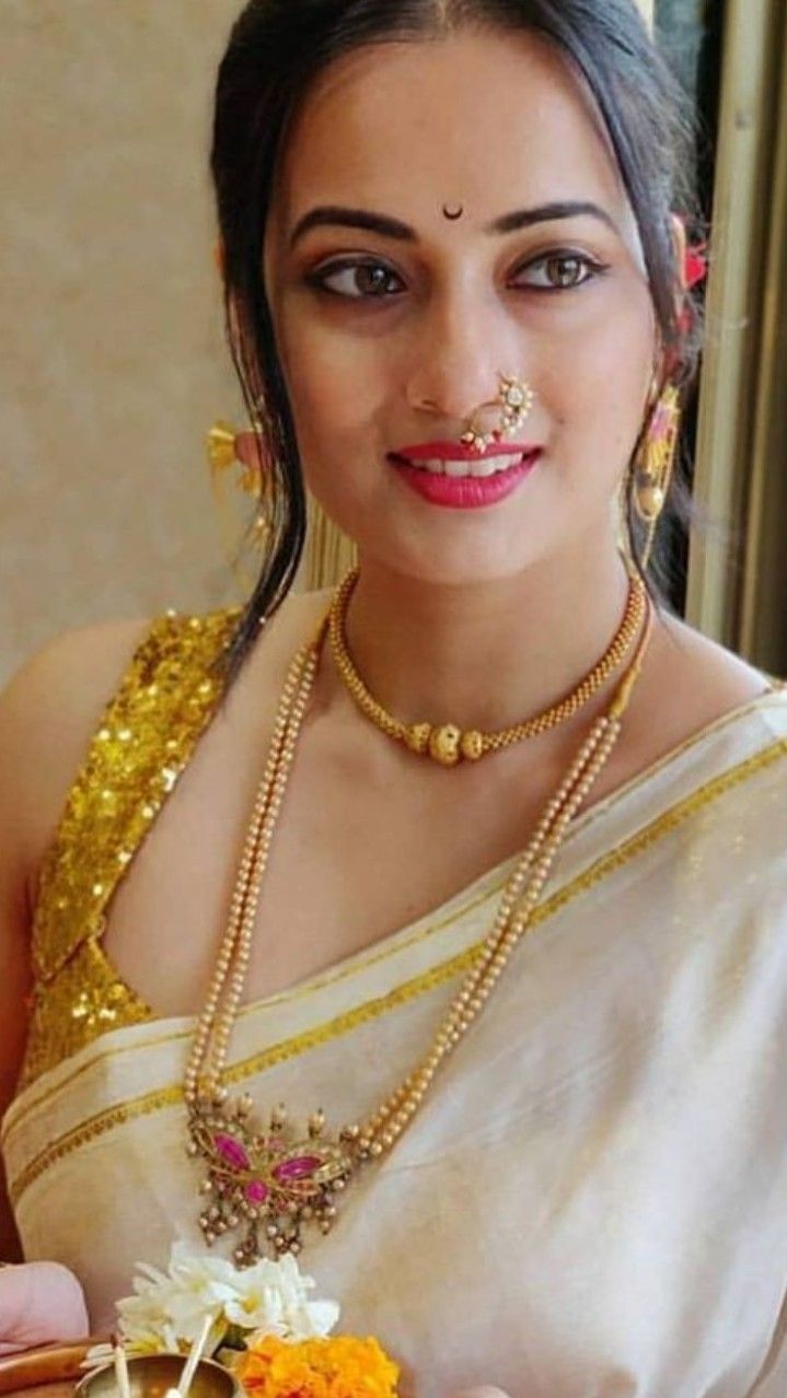 a woman in a white sari holding an orange and yellow flower arrangement with gold jewelry