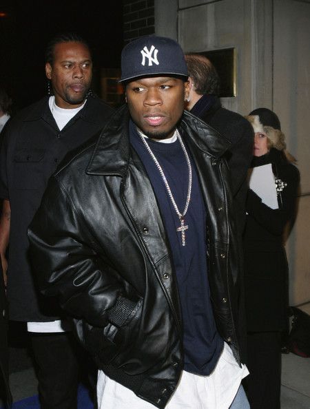 a man wearing a new york yankees hat and black leather jacket standing in front of a crowd