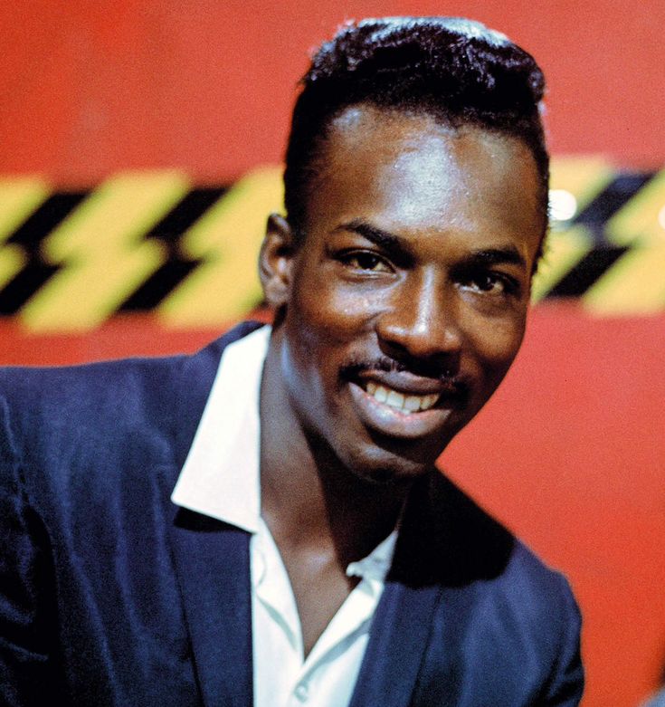 a man in a blue jacket smiles at the camera while standing next to a red and yellow wall