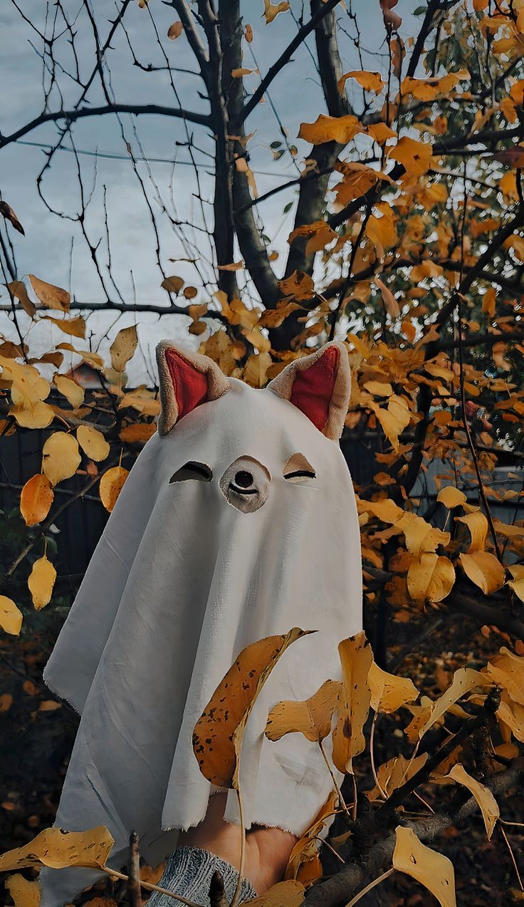 a person holding up a white mask with an animal's face on it in front of some leaves