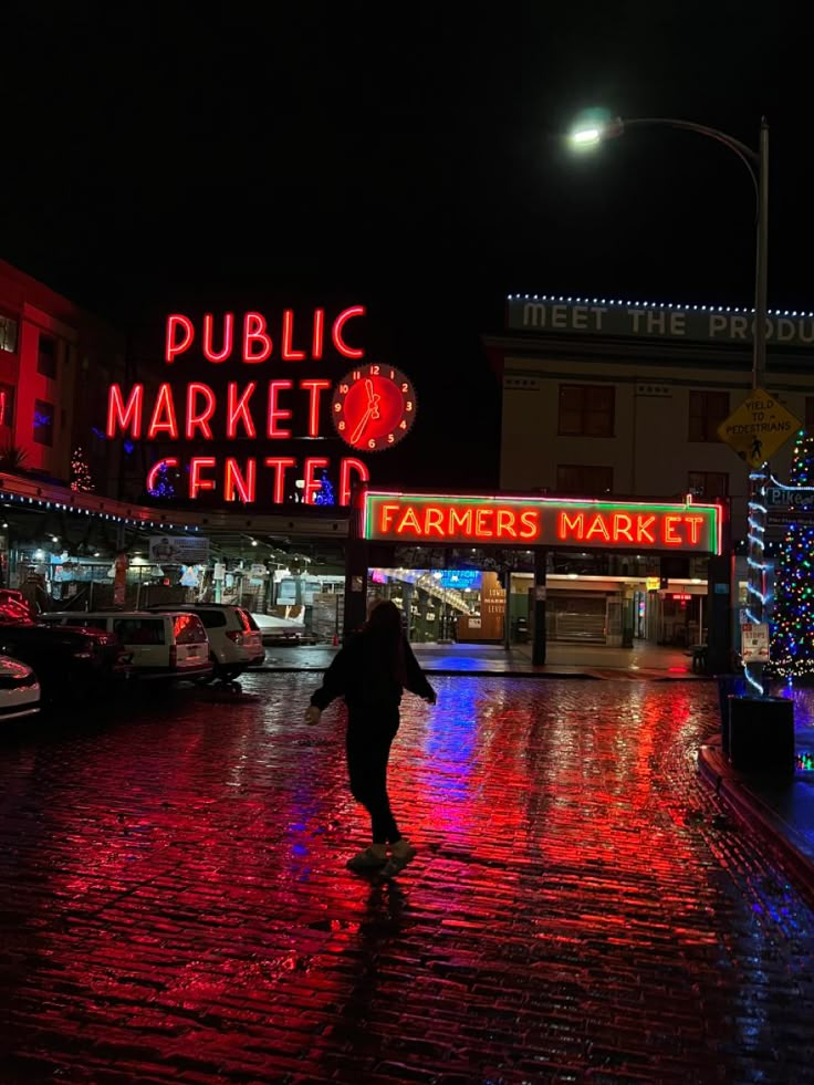 a person walking down a street at night in front of a public market center sign