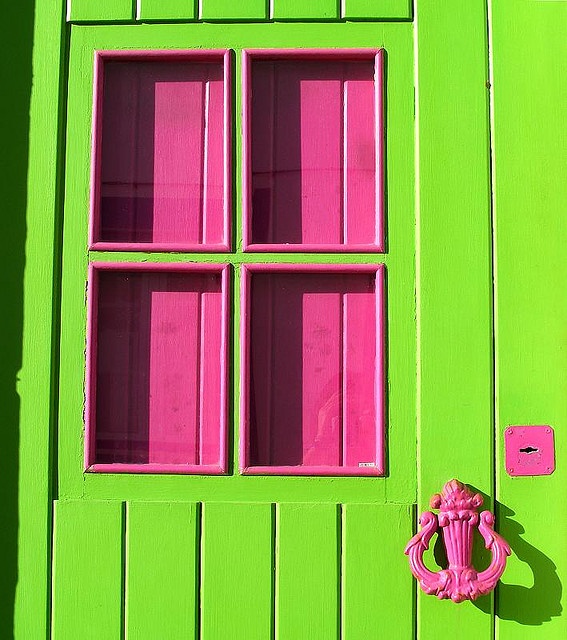 a green window with pink panes on the windowsill and a flower in front of it