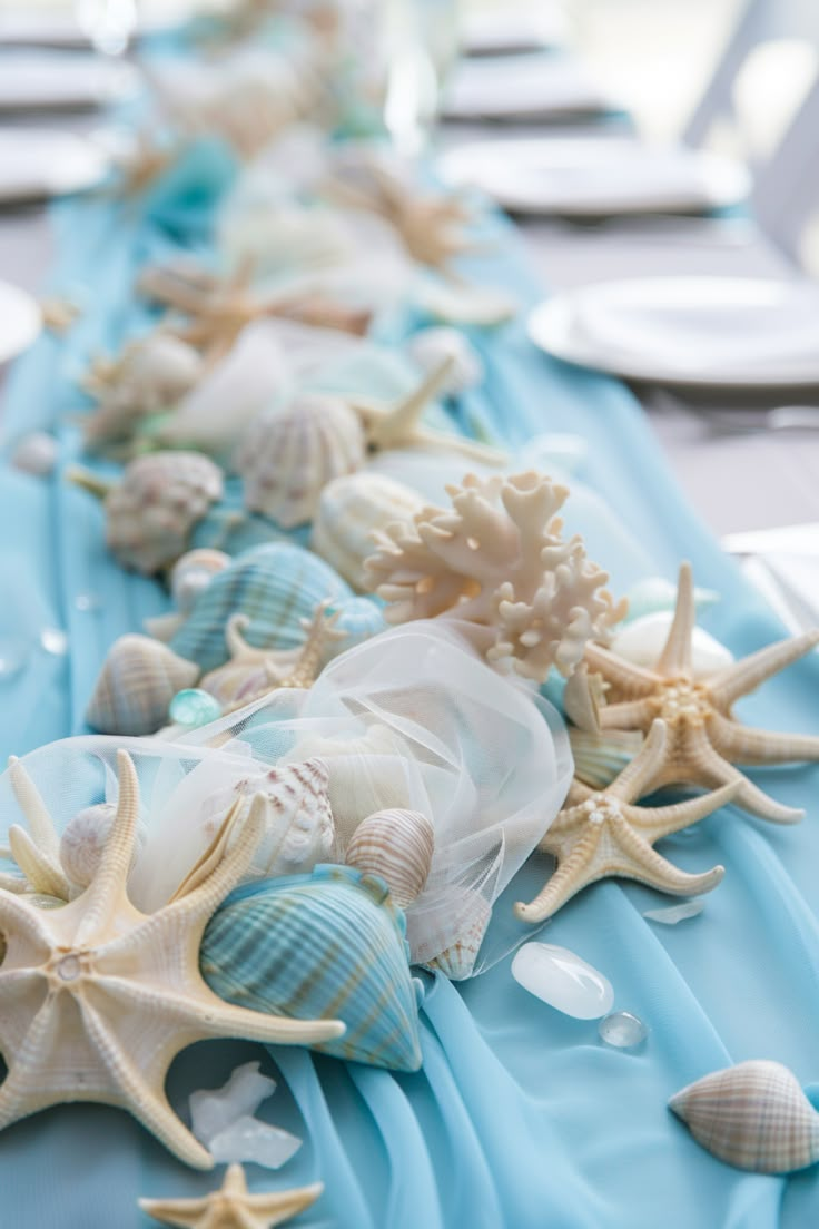 there are many sea shells lined up on the long blue table cloth, along with plates and silverware