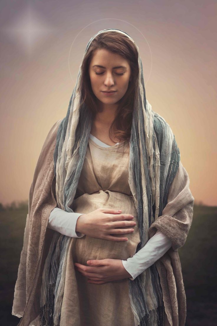 a pregnant woman wearing a shawl and holding her hands on her stomach with the sky in the background