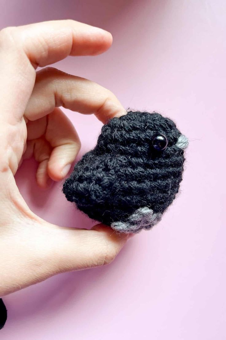 a hand holding a small black and white crochet bird brooch on a pink background