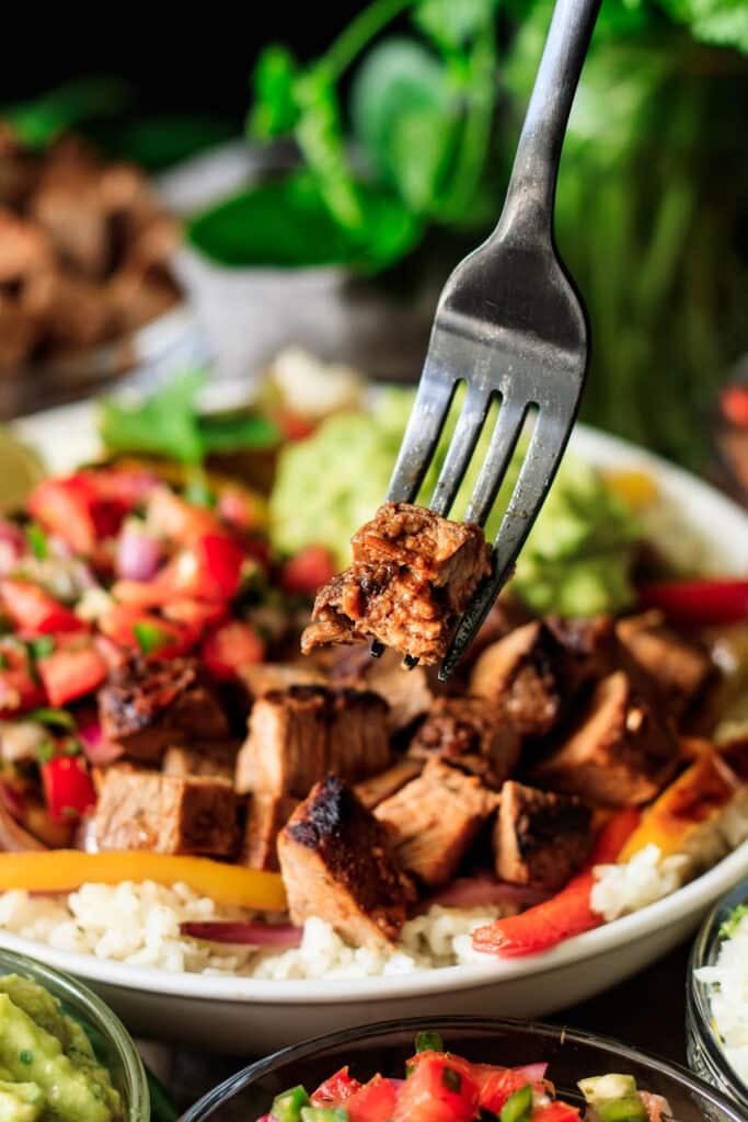 a fork with some meat on it and rice in bowls next to other food items