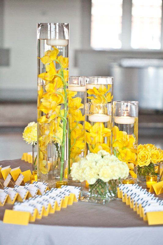 yellow flowers and candles are arranged on a table in front of the centerpieces