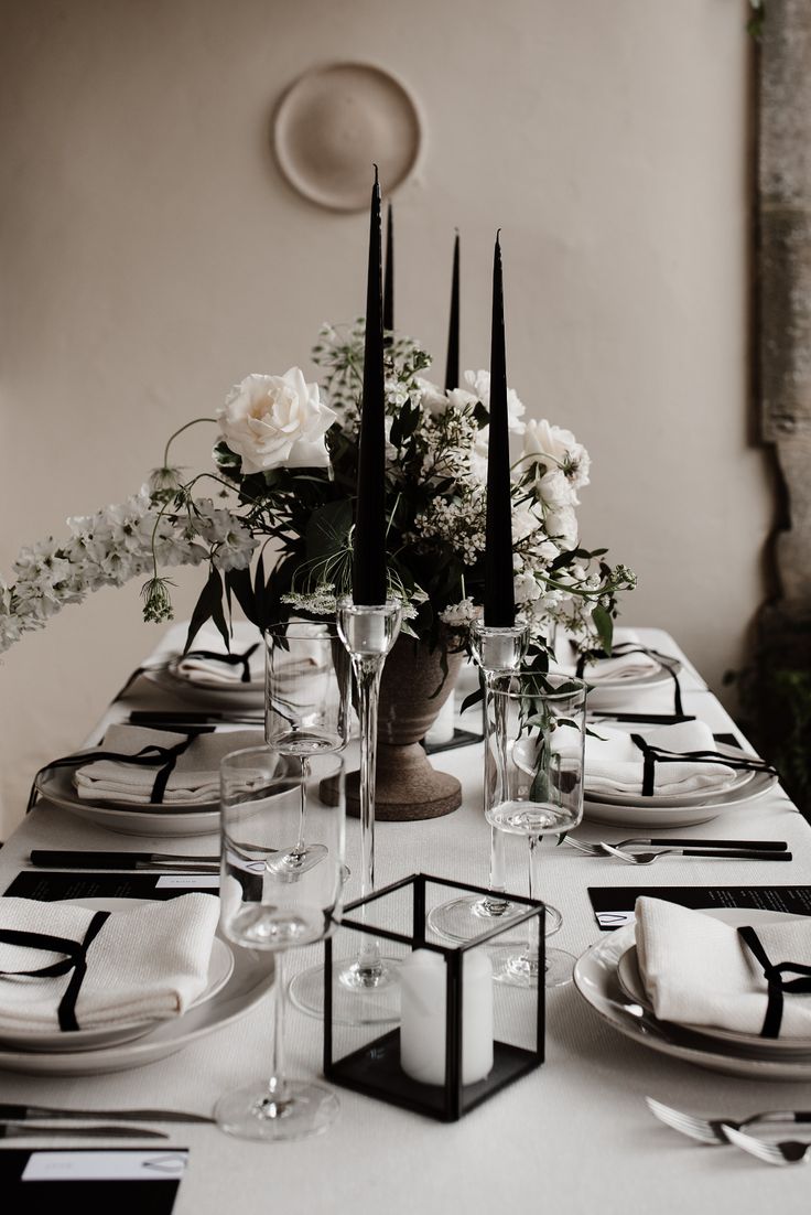 the table is set with black and white place settings, candles, and flowers in vases