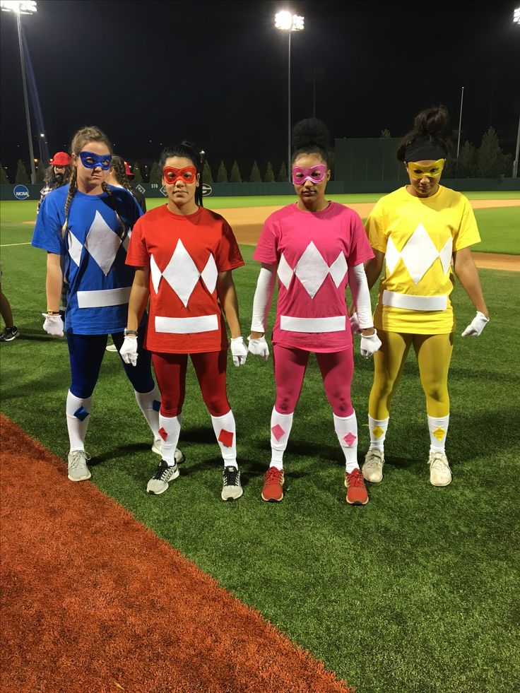 four people in costume standing on a baseball field at night with lights behind them and grass area