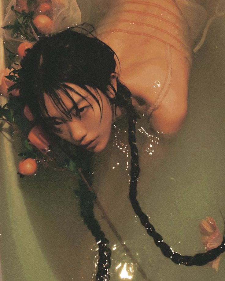 a woman laying in a bathtub filled with water and oranges on the floor