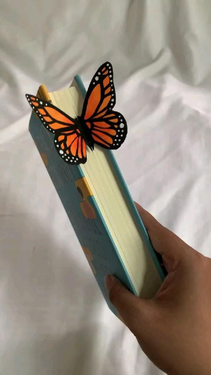 a hand holding an open book with a butterfly on it