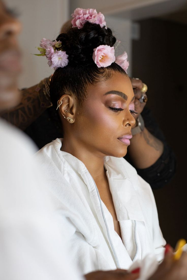 a woman is getting her hair done with flowers in her hair while another man looks on