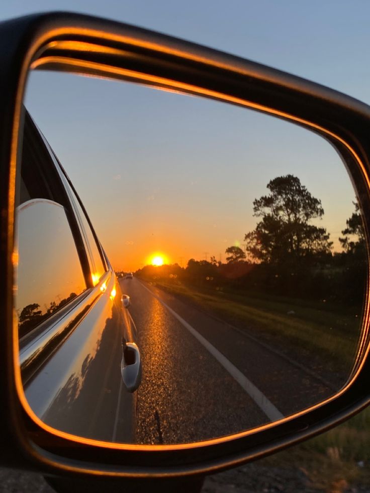 the sun is setting in the side mirror of a car