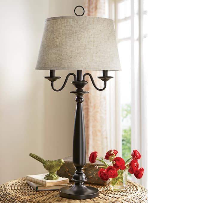 a table with a lamp and some flowers on it next to a book, bird figurine and red roses