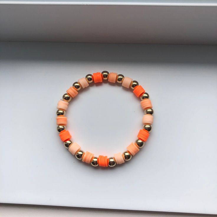 an orange and gold beaded bracelet sits in a white box on the counter top