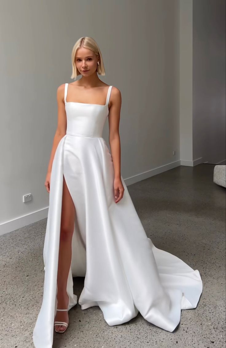 a woman in a white dress standing next to a wall and posing for the camera