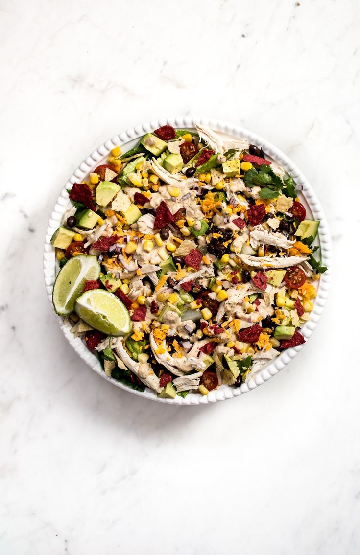 a white bowl filled with salad on top of a marble counter next to a lime wedge